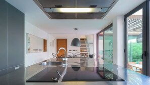 Uma cozinha moderna com ilha central, pia de aço inoxidável e escada que leva a um andar superior.