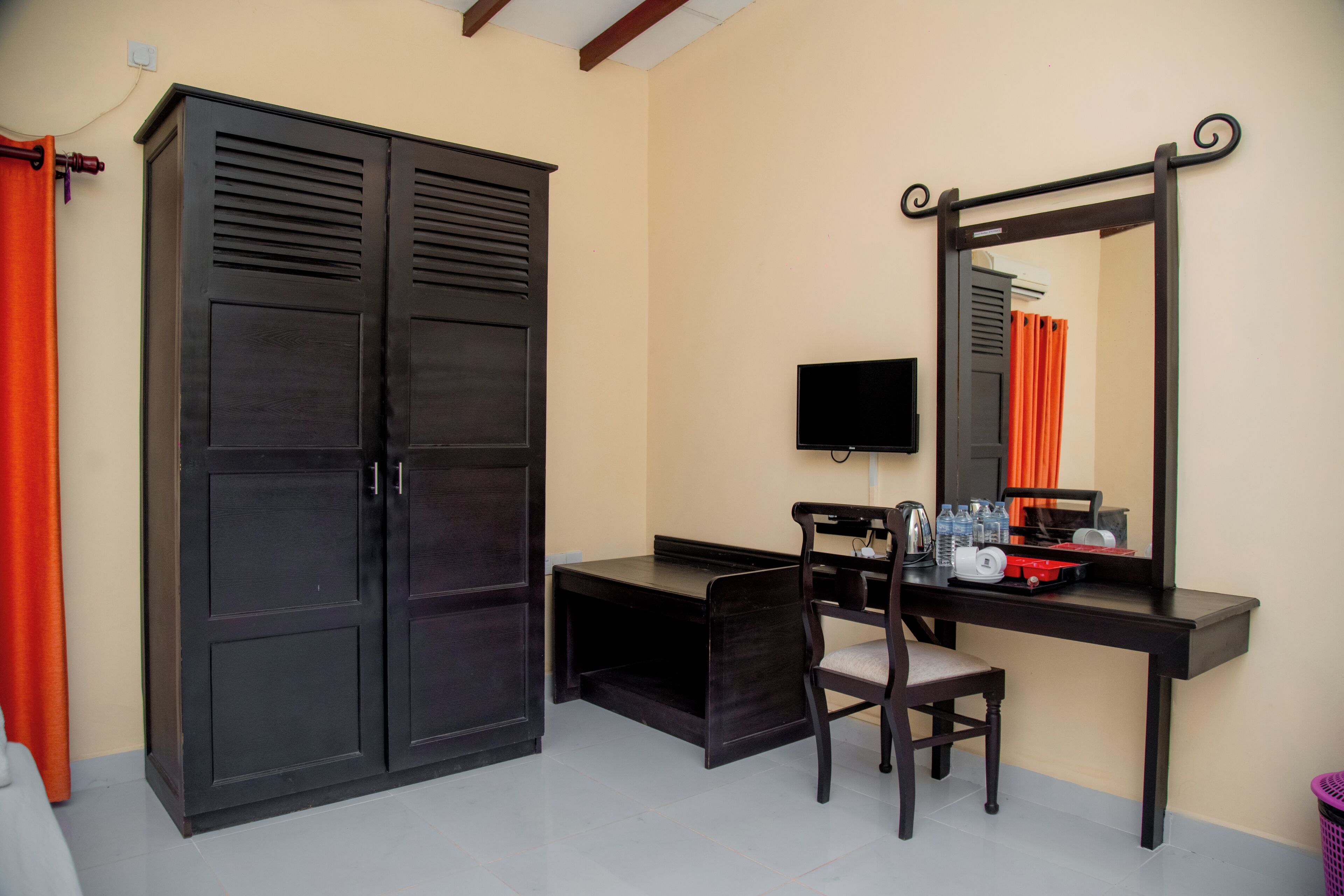 A room with a desk, chair, television, wardrobe, and a mirror.