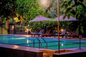Une piscine entourée de verdure, avec des chaises longues et des parasols.