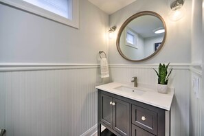 A bathroom with a white vanity, a round mirror, and a potted plant. - Stunning House w/ Deck, Game Room & Home Gym! (Saratoga Springs)