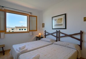 A bedroom with two beds, a window with curtains, a bedside table with a lamp, and a framed picture on the wall. - Apartment 'Calabruix' with Sea View, Wi-Fi and Air Conditioning (Son Serra de Marina)