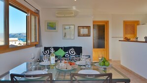 A dining area with a table set for four, a view of the sea through large windows, and a kitchen area with a wooden counter. - Seaside Family Apartment 200 mts from the Beach (Son Serra de Marina)