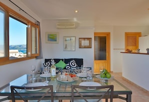 A dining area with a table set for four, a view of the sea through large windows, and a kitchen area with a wooden counter.