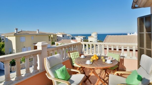 A balcony with a wooden table, chairs, and a view of the sea. - Seaside Family Apartment 200 mts from the Beach (Son Serra de Marina)