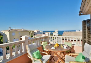 A balcony with a wooden table, chairs, and a view of the sea. - Seaside Family Apartment 200 mts from the Beach (Son Serra de Marina)