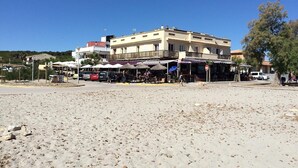 A beachfront building with outdoor seating, a sandy beach in front, and a clear blue sky. - Seaside Family Apartment 200 mts from the Beach (Son Serra de Marina)