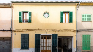 A building with a yellow facade, green shutters, a wooden door, and a small circular window above the door. - Apartment Sa Mina with Terrace & Wi-Fi (Santa Margalida)