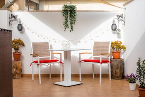 Une terrasse avec deux chaises blanches, une table blanche, des guirlandes lumineuses et des plantes en pot.