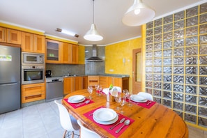Una cocina moderna con armarios de madera, un refrigerador de acero inoxidable y una mesa de comedor preparada para seis personas, con vasos y platos.