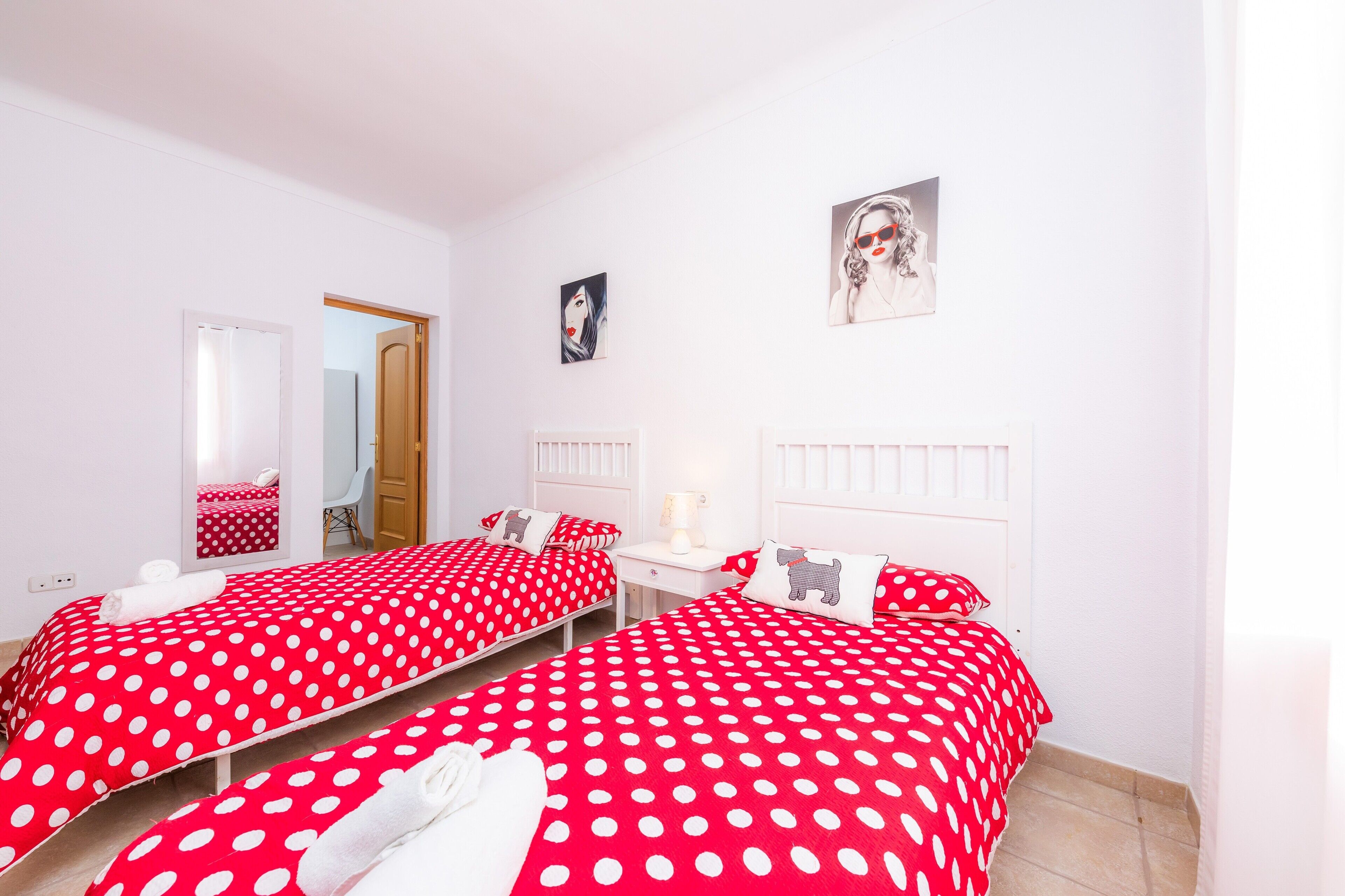 A room with two beds, a mirror, a door, and a wall-mounted picture.
