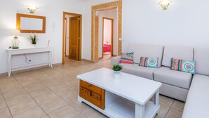 A living room with a white sofa, colorful pillows, a white coffee table, a console table with a mirror, and a plant. - Apartment Sa Mina with Terrace & Wi-Fi (Santa Margalida)