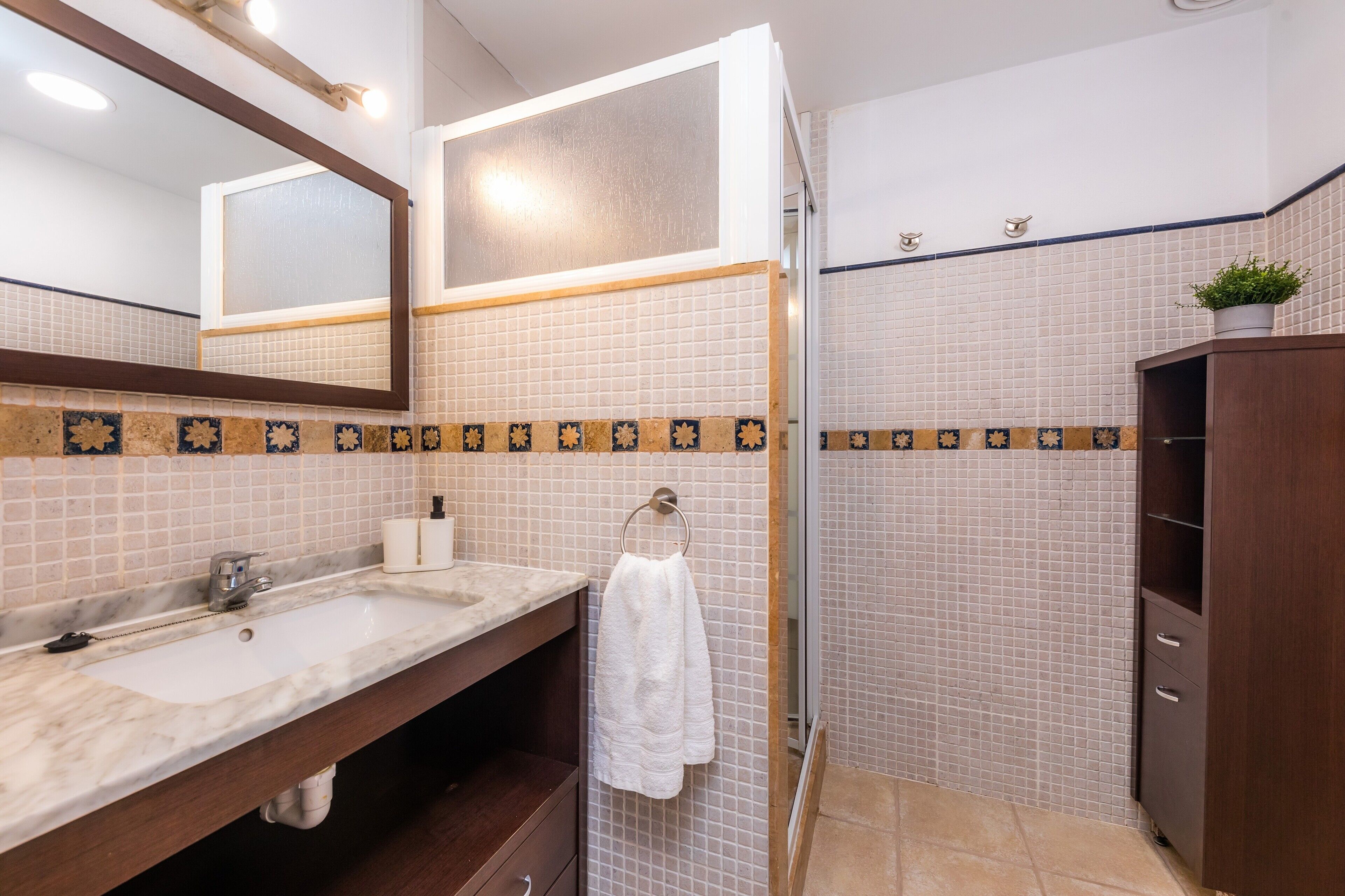 A bathroom with a sink, mirror, towel rack, and a shower area.