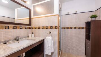 A bathroom with a sink, mirror, towel rack, and a shower area.