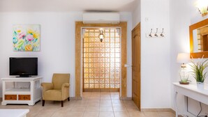 A living room with a TV, a chair, a painting, and a wooden door with a window. - Apartment Sa Mina with Terrace & Wi-Fi (Santa Margalida)