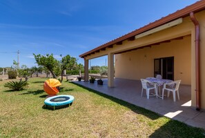 A patio area with a table and chairs, a trampoline, and a covered seating area.
