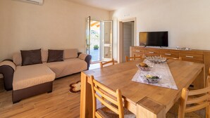 A living room with a sofa, wooden dining table, chairs, a TV, and a kitchen area. - Holiday Home "Casa Vacanza Il Melograno" with 2 Private Terraces, A/C and Wi-Fi (Santa Maria del Focallo)