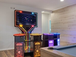 A room with a neon arcade machine, a pool table, and a wooden wall.