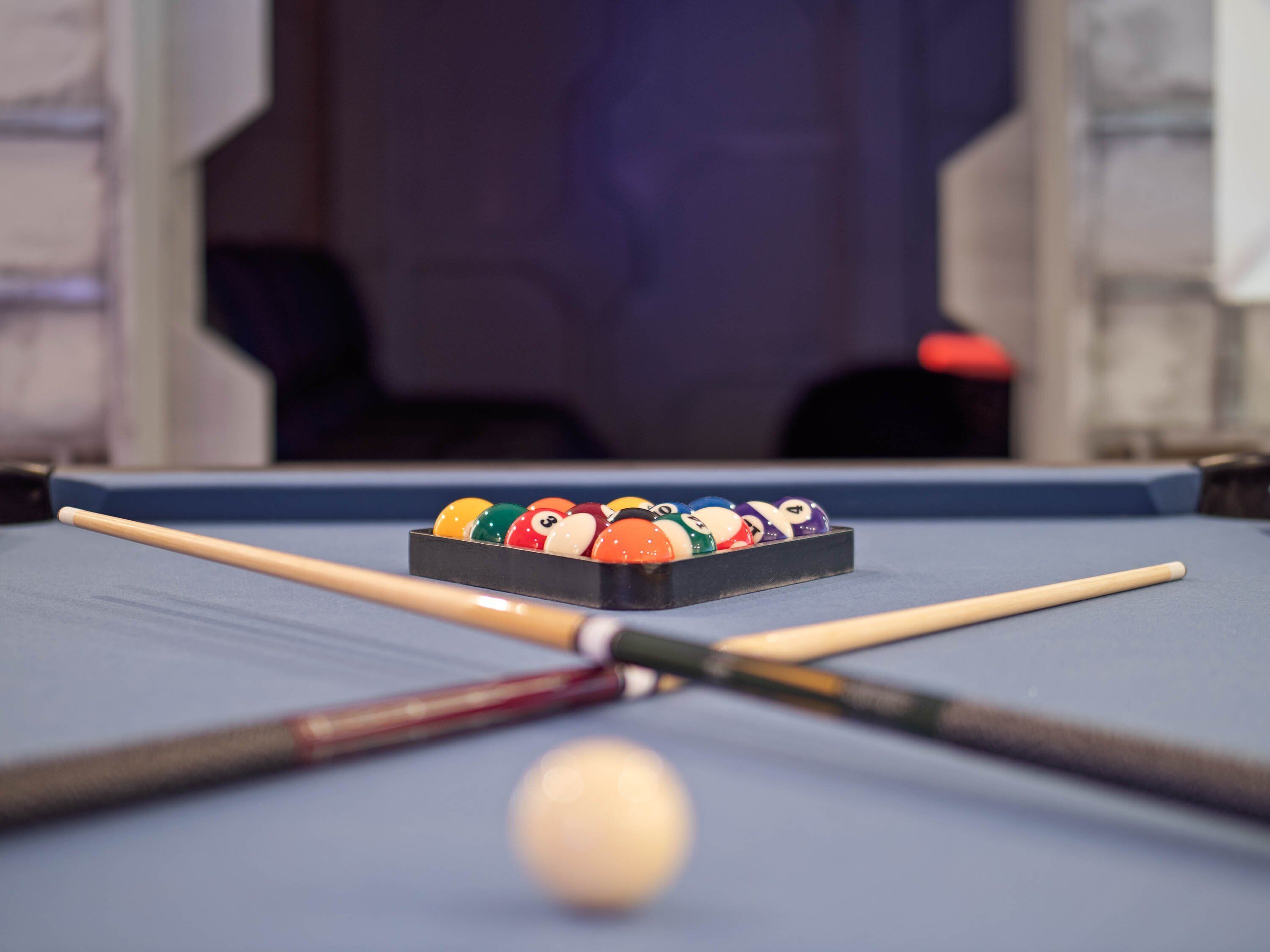 A pool table with a rack of billiard balls and two pool cues.