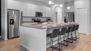A modern kitchen with white cabinets, stainless steel appliances, a granite countertop, and bar stools.