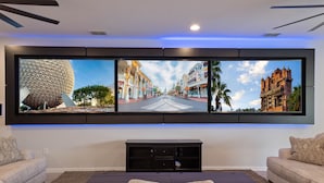 A living room with a large flat-screen TV mounted on the wall displaying three different scenes.