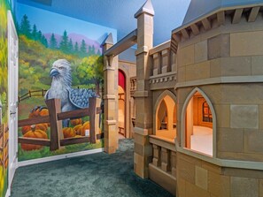 A playhouse with a mural of an eagle and pumpkins, stone walls, and arched windows.