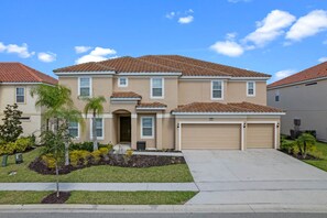 A two-story house with a beige exterior, a brown tiled roof, and a garage with two doors.