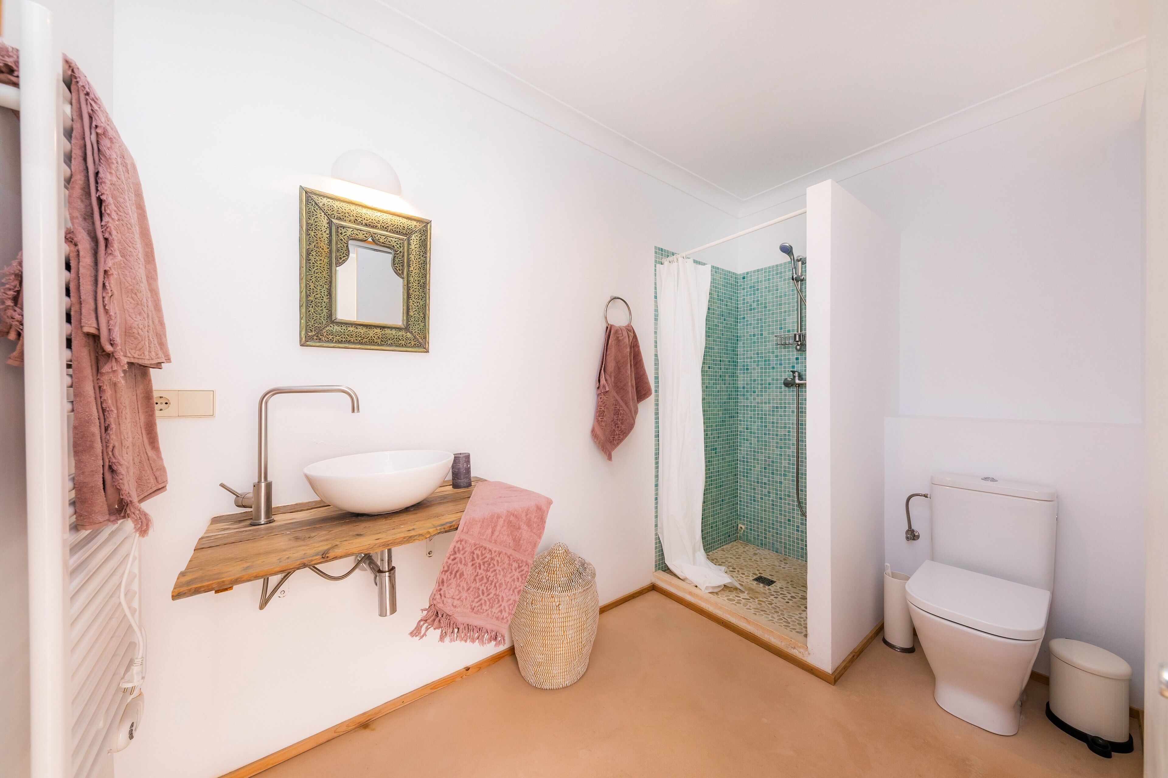 Un baño con lavamanos blanco, un espejo, ducha con pared de azulejos verdes y un inodoro.