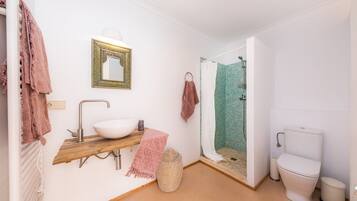 Un baño con lavamanos blanco, un espejo, ducha con pared de azulejos verdes y un inodoro.
