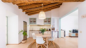 A modern kitchen with white cabinets, a dining table with chairs, and a hanging light fixture.