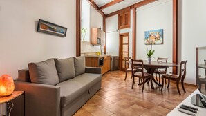 Een woonkamer met een bank, een eettafel met stoelen, een keukenhoek en een televisie.