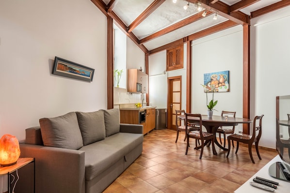 A living room with a sofa, a dining table with chairs, a kitchen area, and a TV.