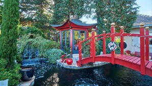 Un pont rouge enjambant un étang, avec un kiosque et une végétation luxuriante.