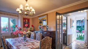 Un coin repas avec une table dressée pour quatre personnes, entourée de chaises, d’un lustre et d’œuvres d’art accrochées aux murs.