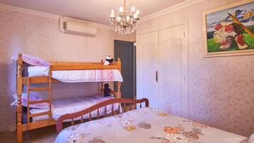 Una camera da letto con un letto a castello, una sedia di legno, un lampadario, una porta e una coperta con motivo floreale.