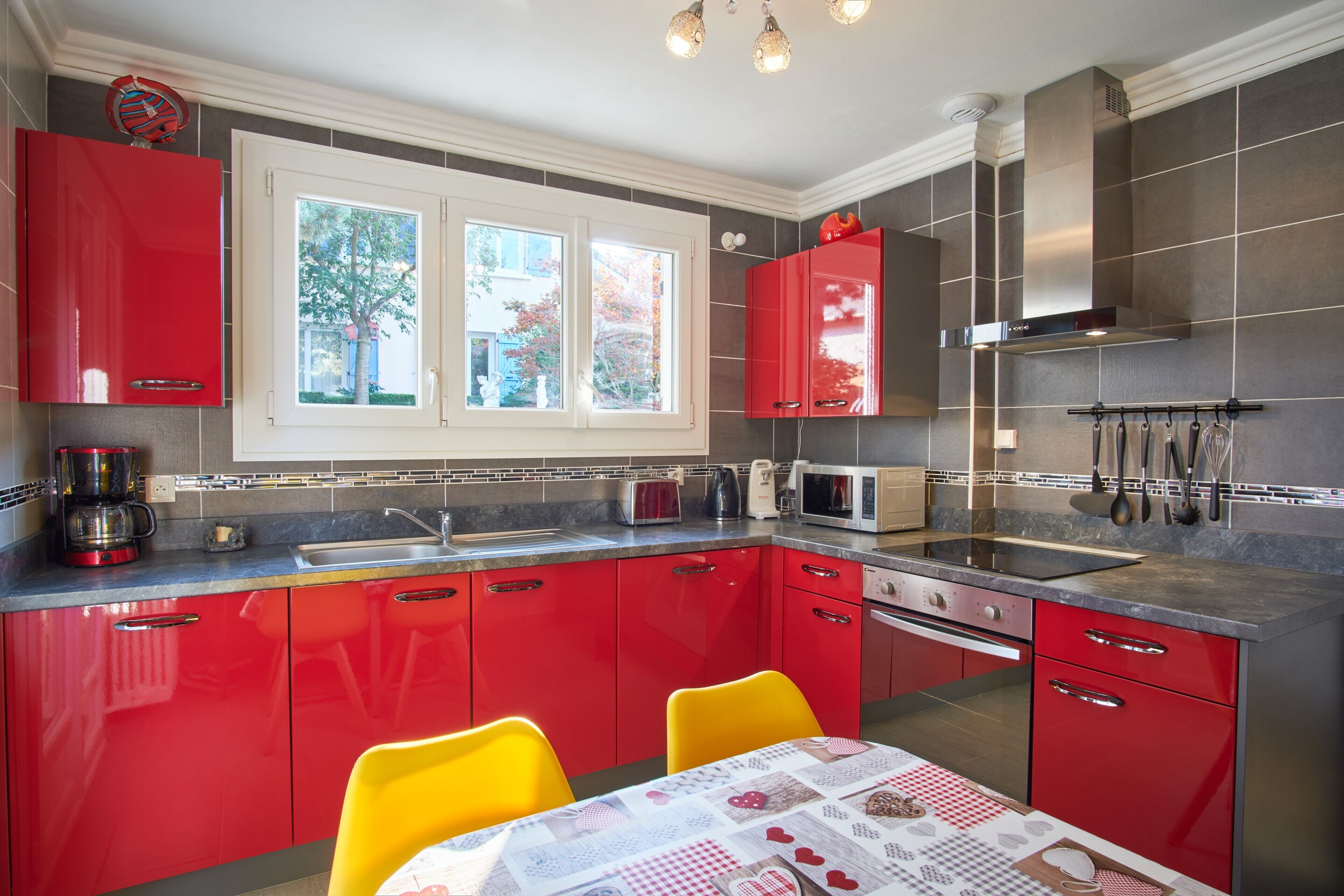 A kitchen with red cabinets, a window, and a table with a checkered tablecloth.