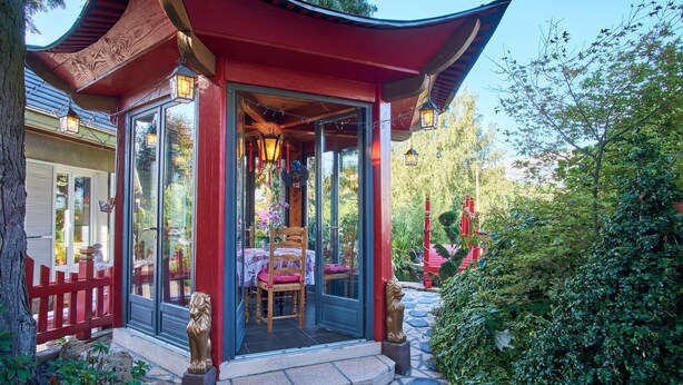 Un bâtiment de style traditionnel, doté d’un porche, d’une clôture en bois peinte en rouge et d’une terrasse carrelée en pierre.