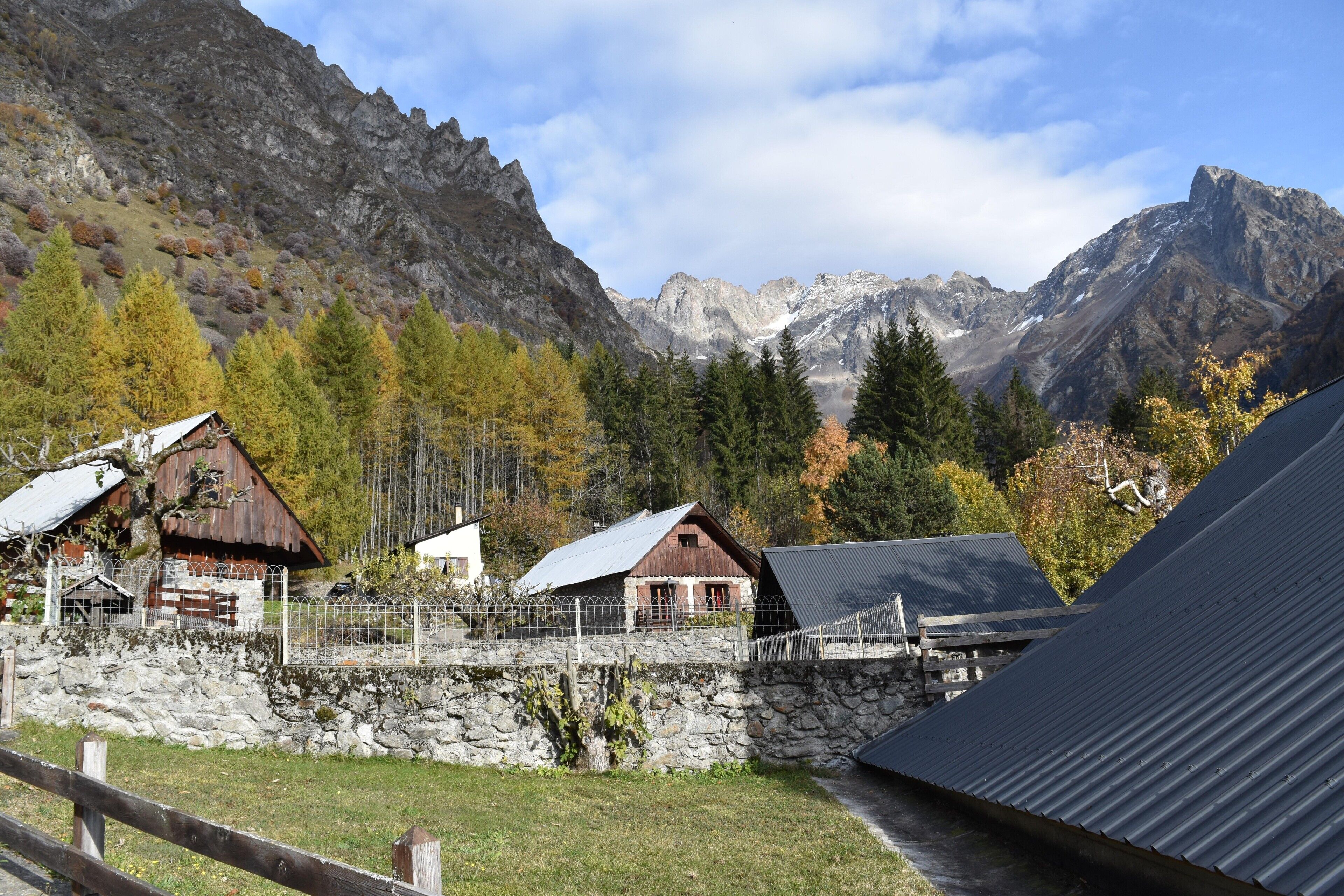 Un paysage de montagne avec des bâtiments rustiques, un mur de pierre et un toit en métal.