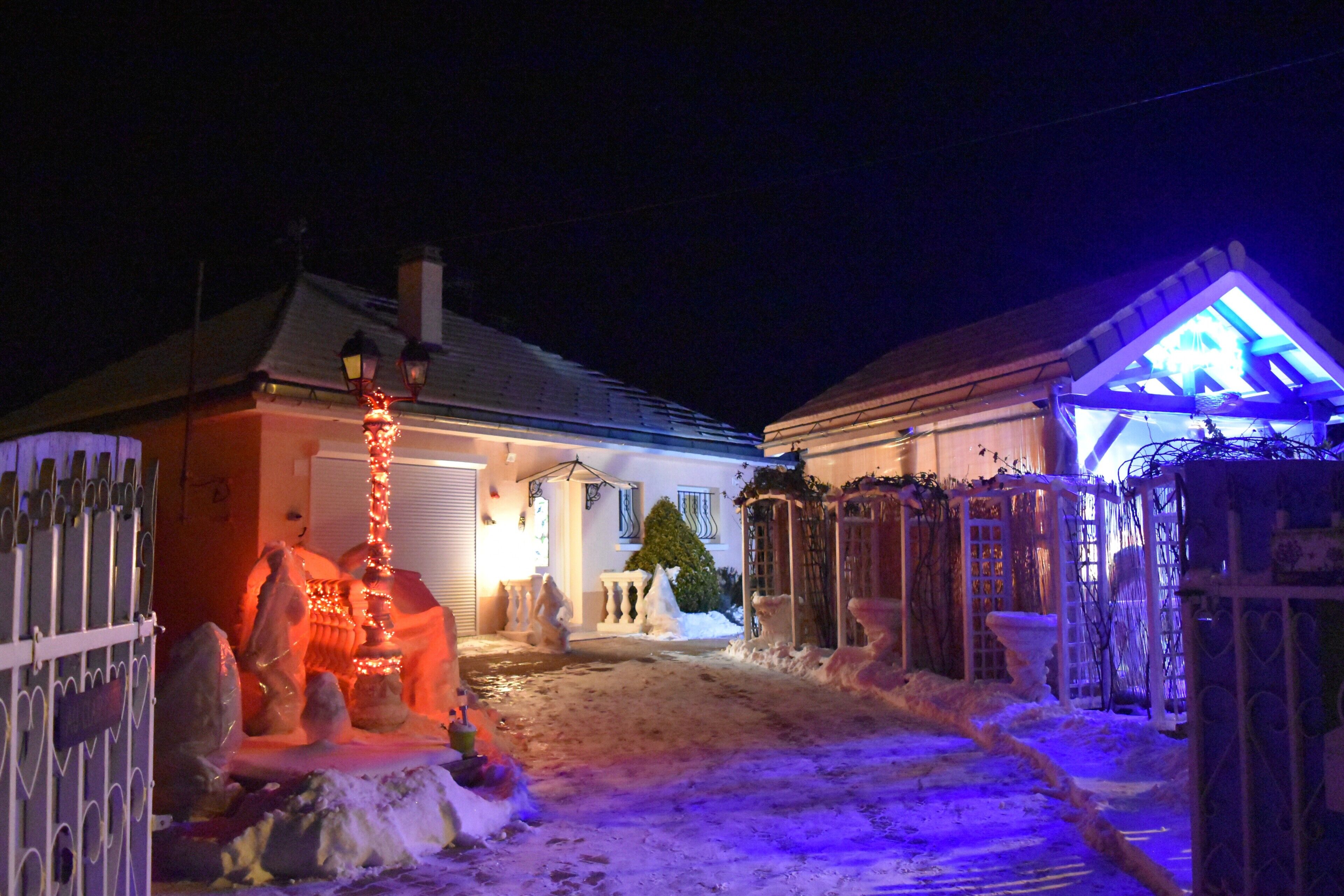 A snow-covered pathway leading to a house with a lit entrance and a snowman decoration.