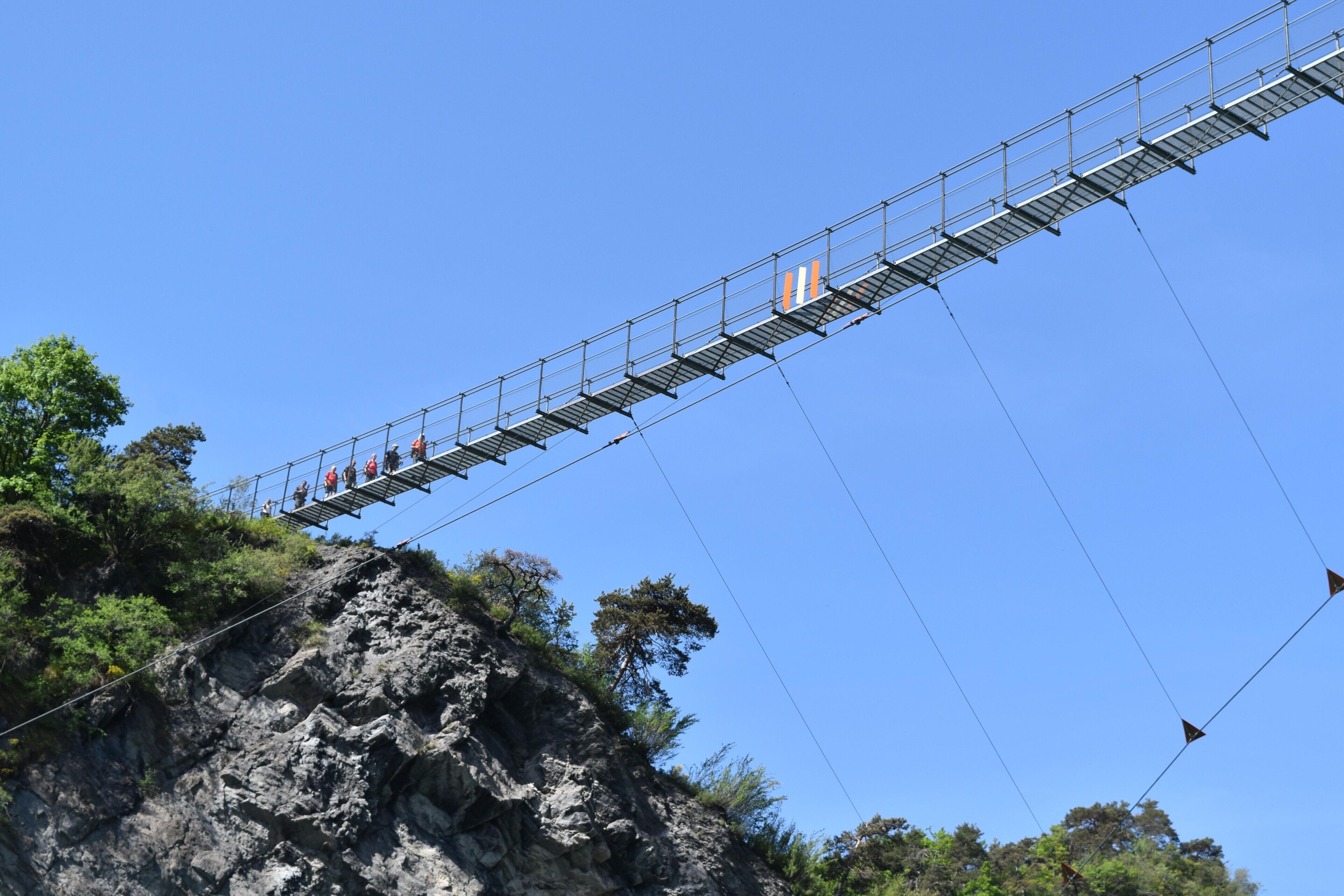 A suspension bridge with a rocky cliff and trees.