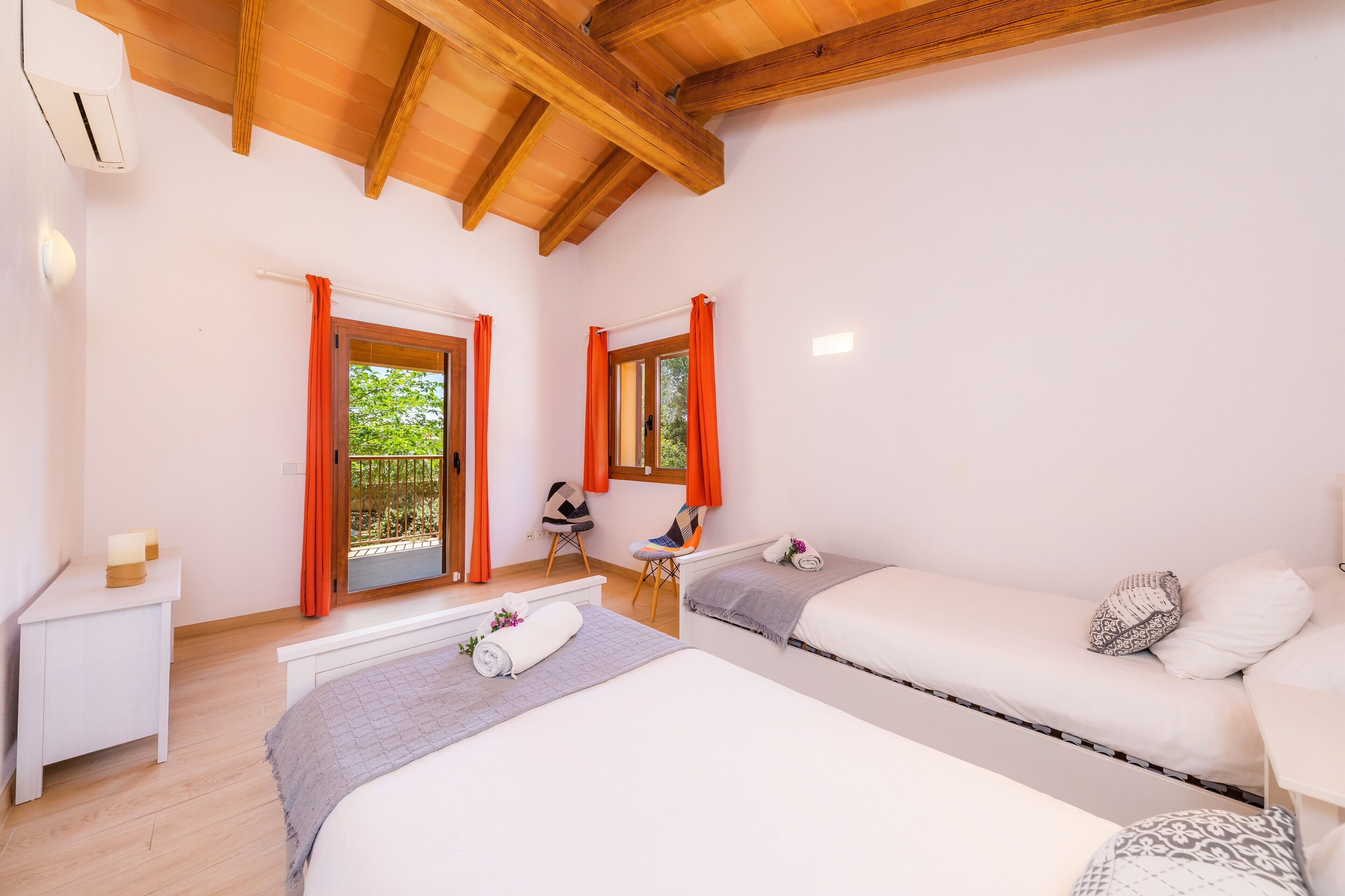 A bedroom with two beds, a bench, a chair, a small table, and a window with curtains.