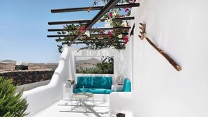 Um quarto de paredes brancas com um sofá azul, uma mesa redonda pequena e uma estrutura de madeira suspensa com flores.