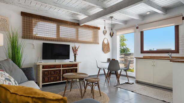 Uma sala de estar moderna com televisão, mesa de jantar, cadeiras e uma área de cozinha com janela.