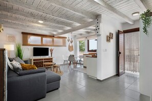 A modern living room with a grey sofa, a TV, and a dining area with a table and chairs.