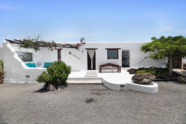A modern white building with a patio, a wooden bench, and a rock centerpiece.