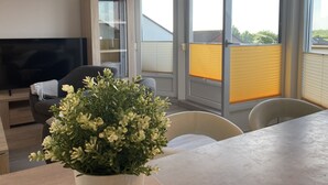A modern living room with a flat-screen TV, a sofa, a dining table, and a potted plant. - Apartment house "Charibi" a well-kept residential complex near the beach (Dahme)