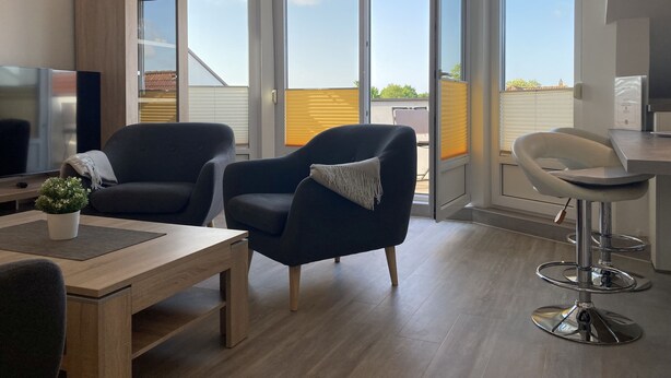 A modern living room with a wooden table, two armchairs, a TV, and a balcony with large windows. - Apartment house "Charibi" a well-kept residential complex near the beach (Dahme)