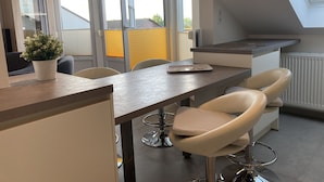 A modern kitchen with a dining area, featuring a long table, bar stools, and a potted plant. - Apartment house "Charibi" a well-kept residential complex near the beach (Dahme)