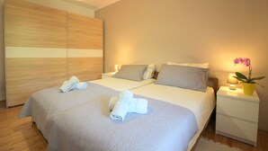 Un lit double avec deux oreillers, une table de chevet avec une lampe et une plante en pot, et une armoire en bois.