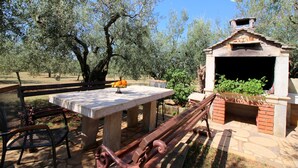Une terrasse extérieure avec une table en pierre, des chaises en métal et un four en briques.