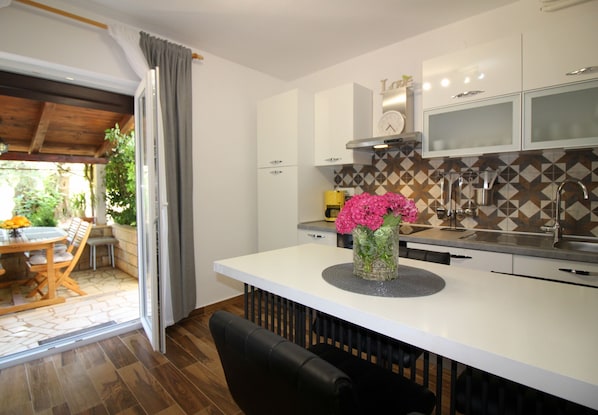 Uma cozinha moderna com armários brancos, uma ilha central com um vaso de flores e uma área de jantar com mesa e cadeiras.